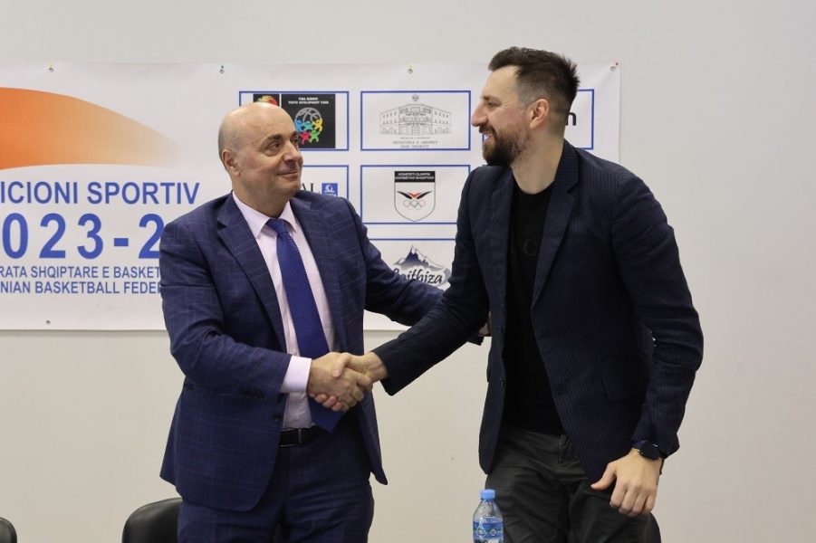 Two men shaking hands in front of a poster

Description automatically generated